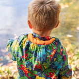 The back of a toddler wearing the Frugi be hoppy puddle buster coat showing the hood detail and orange fleece inside liner.