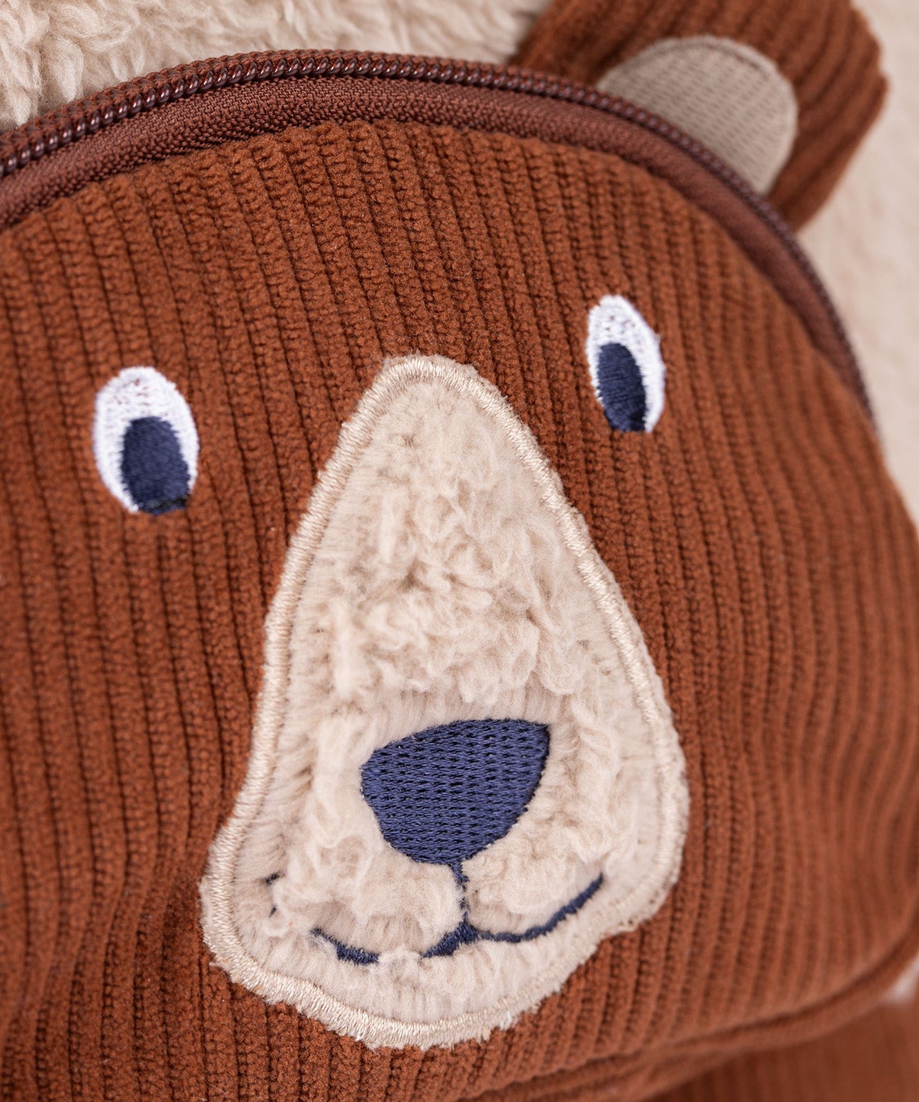 A close up of the  Frugi kids beary wild backpack. Showing the brown corduroy brown bear face detail - features a neutral colour nose trim