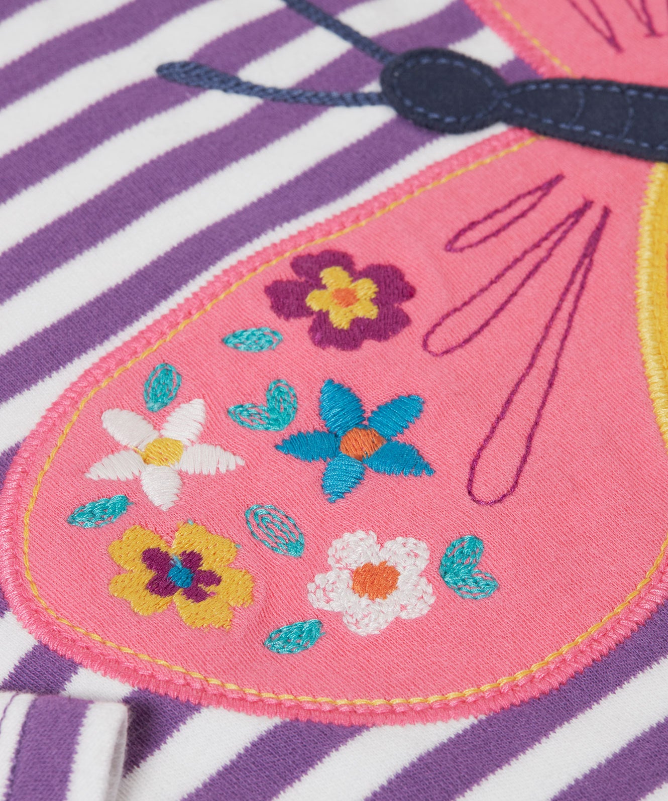 A close up of the embroidered details on the wings of the butterfly applique detail on the front of the Frugi Children's organic cotton Bobby butterfly Applique purple striped  long sleeved Top. The top has a violet purple and white stripe background with a large decorated butterfly applique on the front. This top is a part of a wide range of organic cotton clothing for children available here at Babipur.