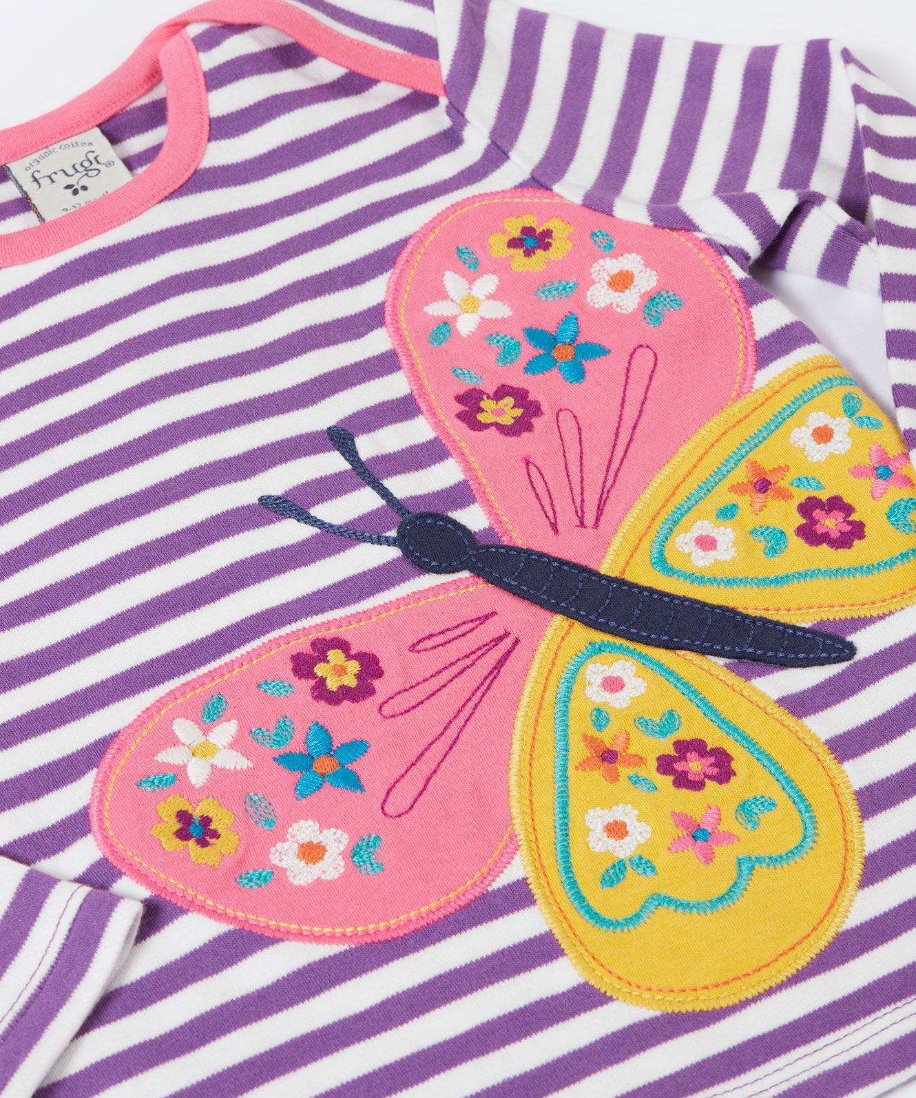A close up of the butterfly applique detail on the front of the Frugi Children's organic cotton Bobby butterfly Applique purple striped  long sleeved Top. The top has a violet purple and white stripe background with a large decorated butterfly applique on the front. This top is a part of a wide range of organic cotton clothing for children available here at Babipur.