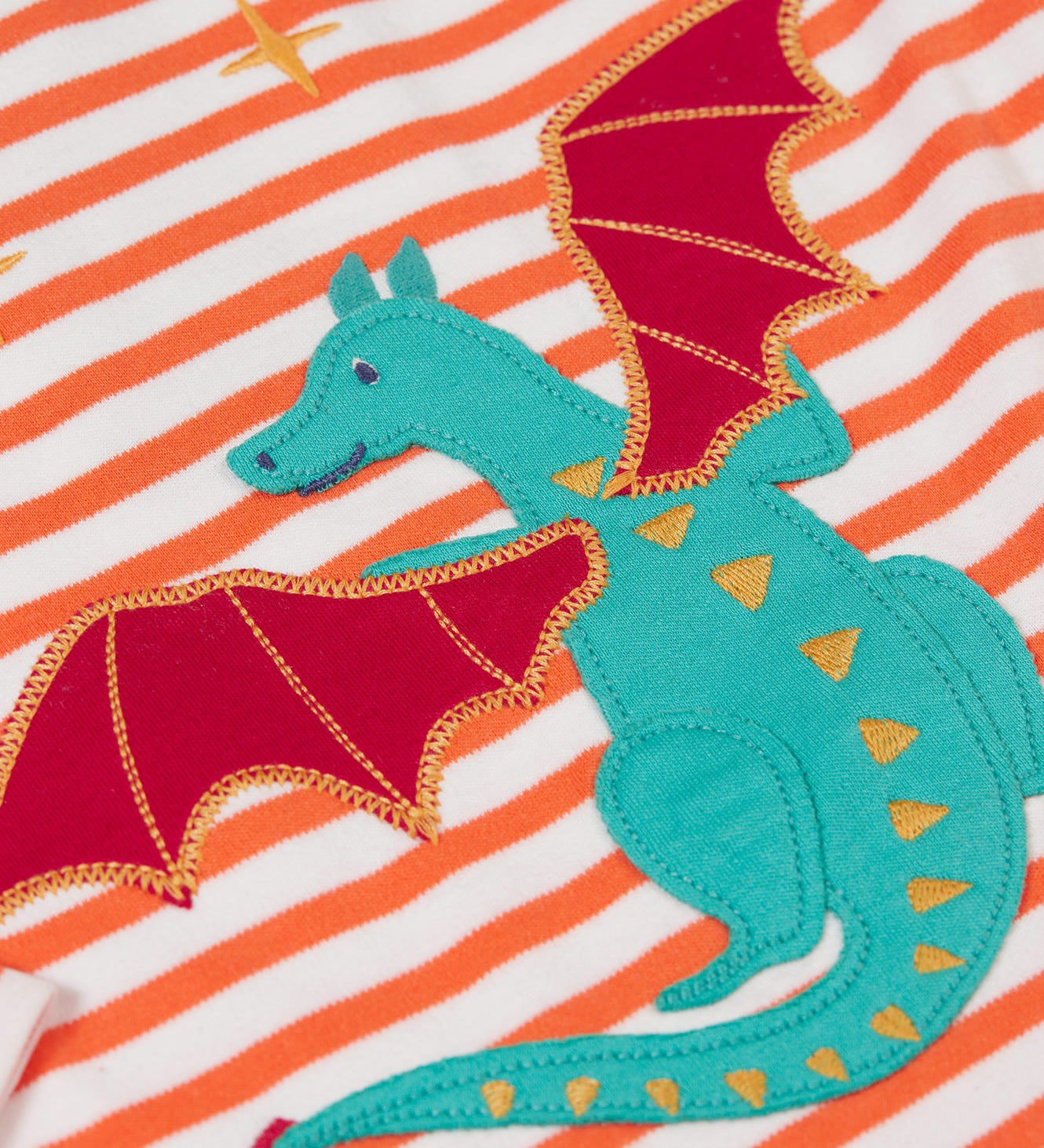 A close up of the Dragon applique on the Frugi Children's Bobby dragon Applique orange and white striped long sleeved Top. This top is a part of a wide range of organic cotton clothing for children available here at Babipur.