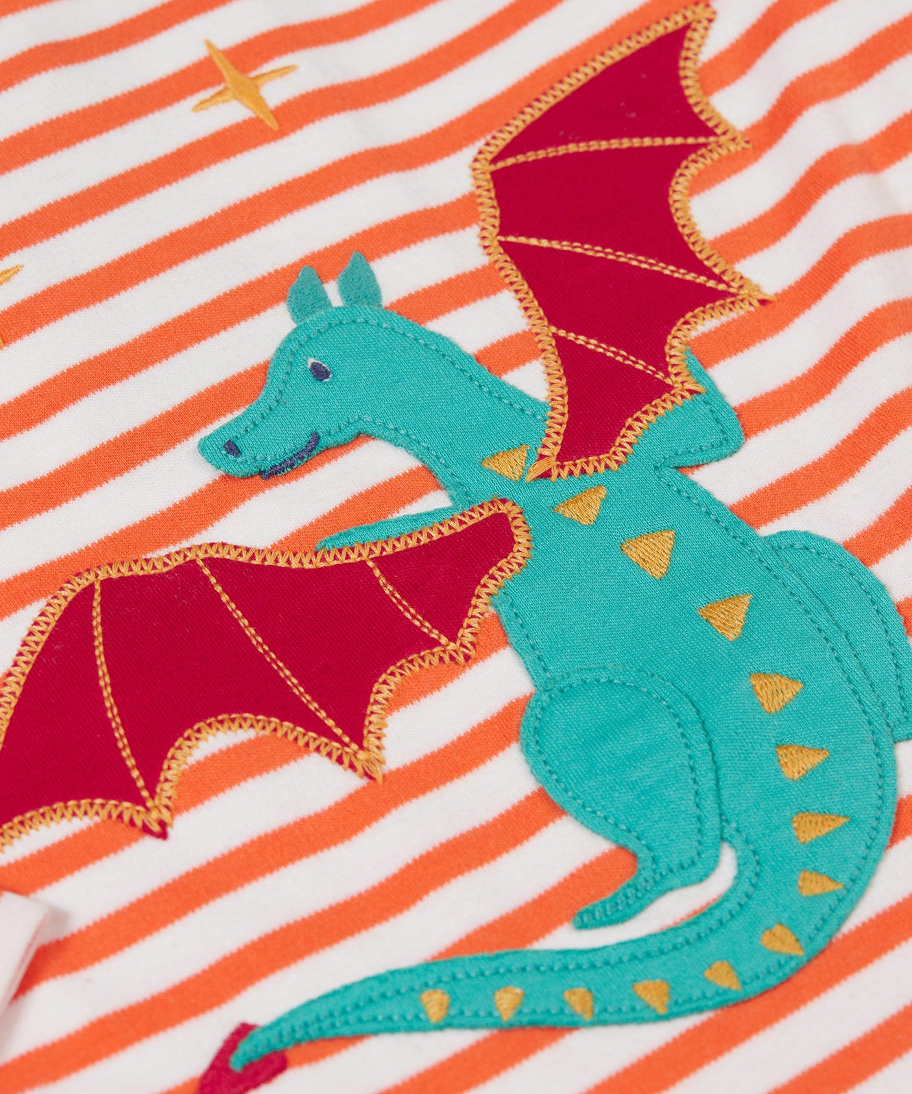 A close up of the Dragon applique on the Frugi Children's Bobby dragon Applique orange and white striped long sleeved Top. This top is a part of a wide range of organic cotton clothing for children available here at Babipur.