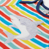 A close up of Frugi Bobster Applique T-Shirt in a Sea Rainbow Stripe print, featuring an embroidered Shark in the centre, and popper fastenings at the top.