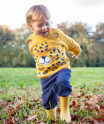 A child walking on grass wearing the Frugi Caleb Leopard Character Knit Jumper, navy cord trousers and yellow wellington boots. This knitted jumper is a part of a wide range of organic cotton clothing for children available here at Babipur.