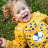 A child laying on grass wearing the Frugi Caleb Leopard Character Knit Jumper. This knitted jumper is a part of a wide range of organic cotton clothing for children available here at Babipur.