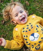 A child laying on grass wearing the Frugi Caleb Leopard Character Knit Jumper. This knitted jumper is a part of a wide range of organic cotton clothing for children available here at Babipur.