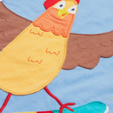 Close up of the Frugi kids cornflower blue chicken t-shirt. Showing the appliqué detail of a brown chicken standing on a skateboard on light blue organic cotton fabric