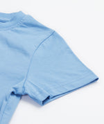 Close up of the Frugi kids cornflower blue chicken t-shirt. Showing short sleeve detail on light blue organic cotton fabric