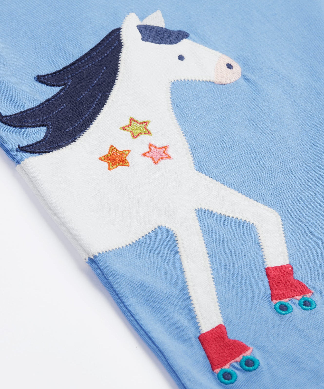 Close up of the Frugi kids cornflower blue, horse t-shirt. Showing the front half appliqué detail on light blue organic cotton fabric.