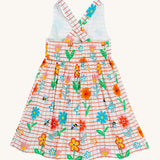 Frugi kids Delpi paint a floral dress - GOTS organic cotton kids dress with white check and red outline, sleeveless with a back strap fasteners the back of the waist band. Features prints of different coloured flowers and bees.