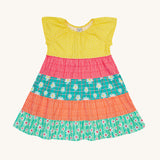 Frugi Dorothy Twirly Dress laid flat, with a  Rainbow Hotchpotch print, a patchwork type design featuring yellow, red orange and green patterns with daisies.
