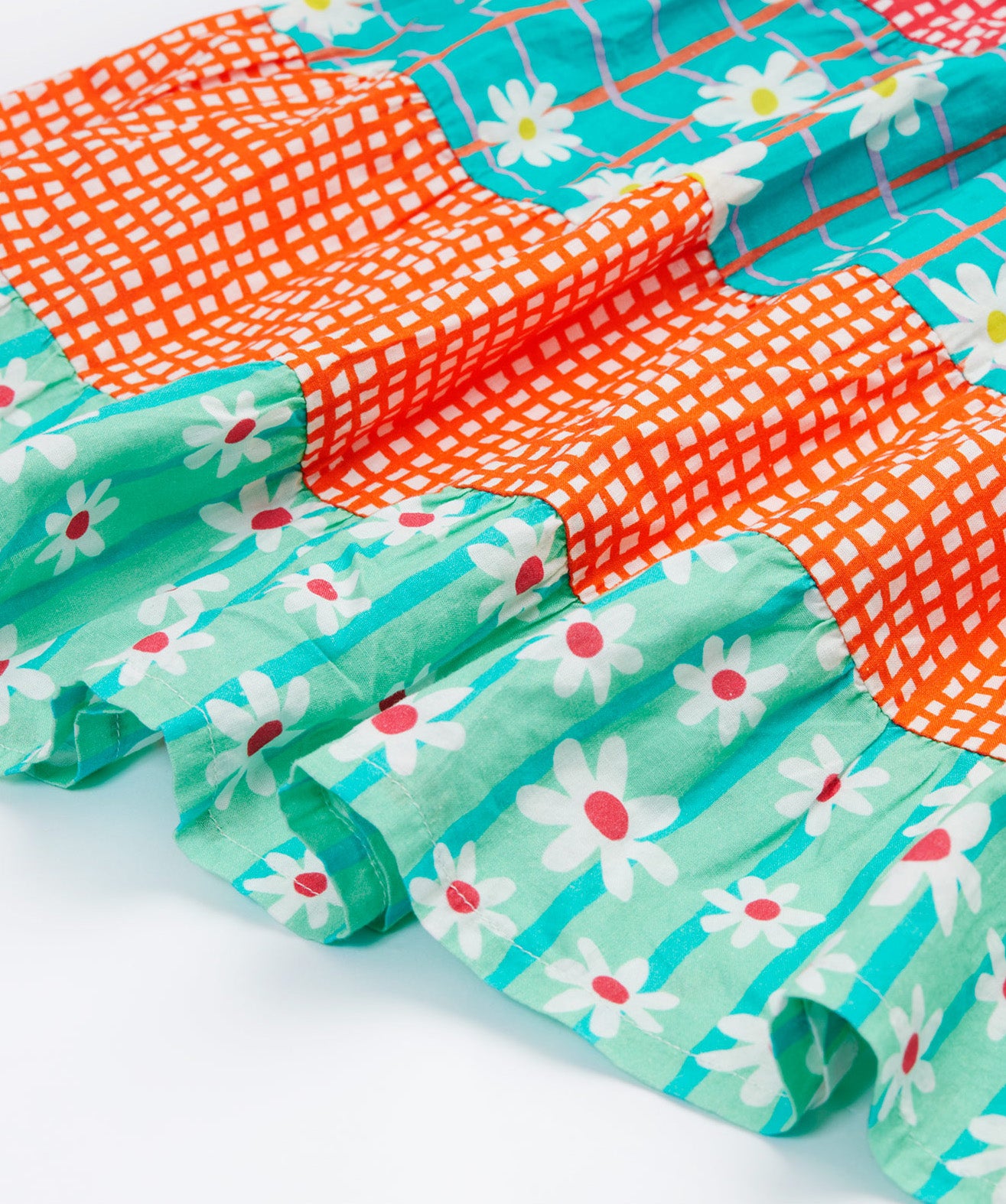 A close up of Frugi Dorothy Twirly Dress, with a Rainbow Hotchpotch print, a patchwork type design featuring orange, mint and green patterns with daisies.