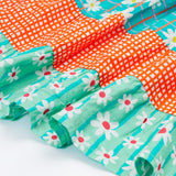 A close up of Frugi Dorothy Twirly Dress, with a Rainbow Hotchpotch print, a patchwork type design featuring orange, mint and green patterns with daisies.