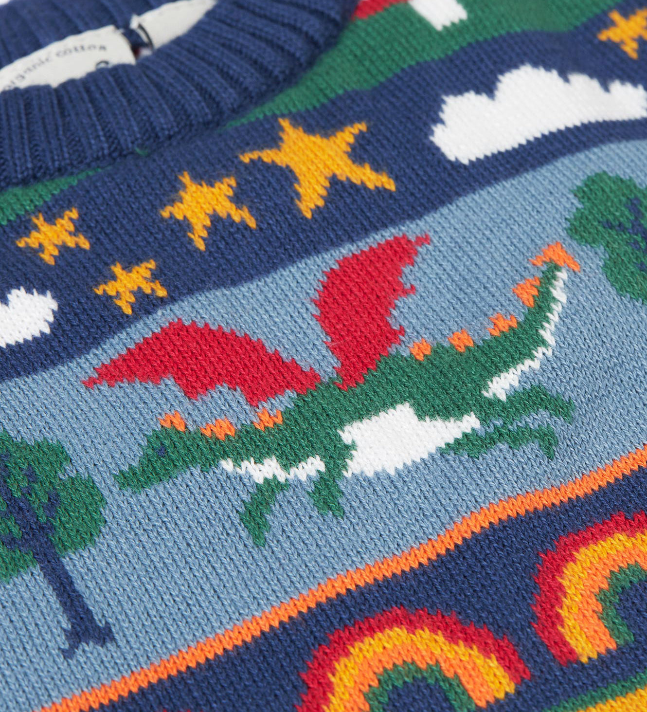 A close up of the green dragon on the Frugi Dragon Fair Isle Organic Cotton Knitted Sweater Vest. A colourful design featuring dragons, rainbows, clouds, stars, toadstools and castles. This sweater vest is a part of a wide range of organic cotton clothing for children available here at Babipur.