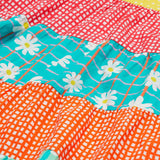 A close up of Frugi Dorothy Twirly Dress, with a Rainbow Hotchpotch print, a patchwork type design featuring orange, mint, red, yellow and green patterns with daisies.