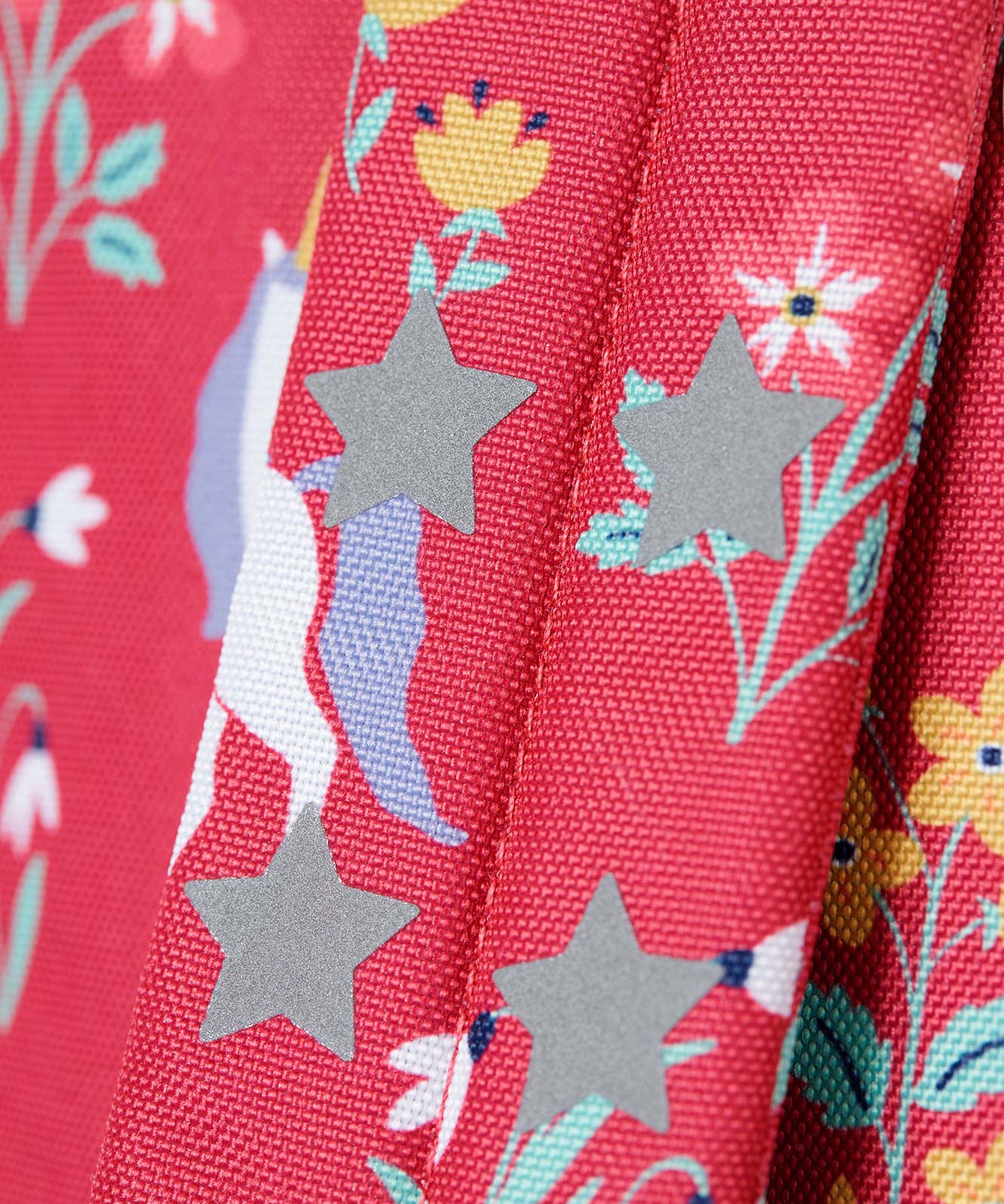 A close up of the shoulder strap on the Frugi rose unicorn floral explorer backpack showing the reflective stars detail.