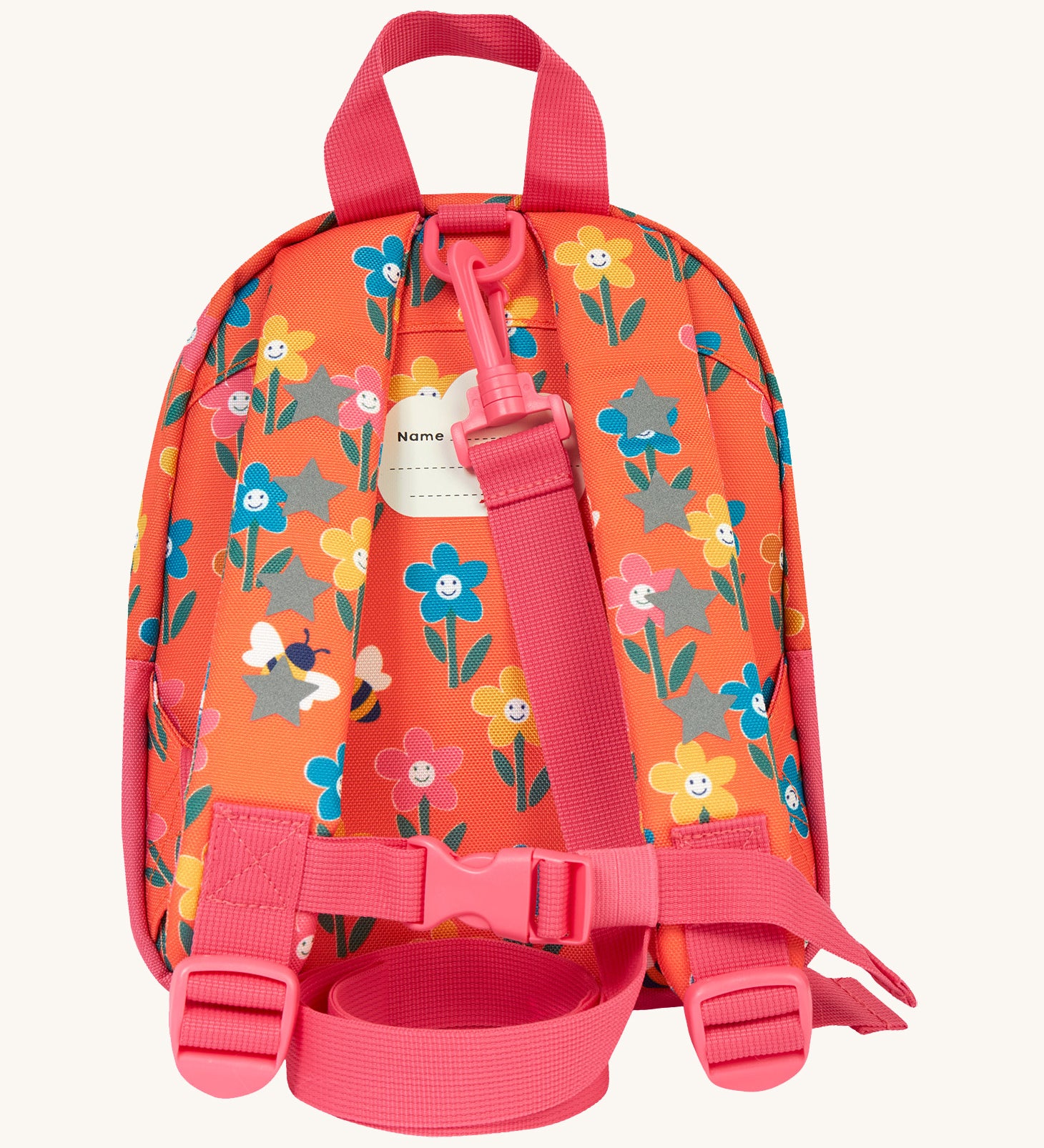 The back of the Frugi little adventures fun flowers backpack showing the reflective stars on the shoulder straps and the pink rein clipped to the top of the bag