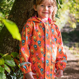 A toddler standing by a tree and wearing the Frugi puddle buster yellow trousers, fun flowers coat.  An orange waterproof coat with playful prints of flowers.