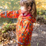 A side view of a toddler wearing the Frugi fun flowers puddle buster coat showing the hood detail and pink fleece inside liner.