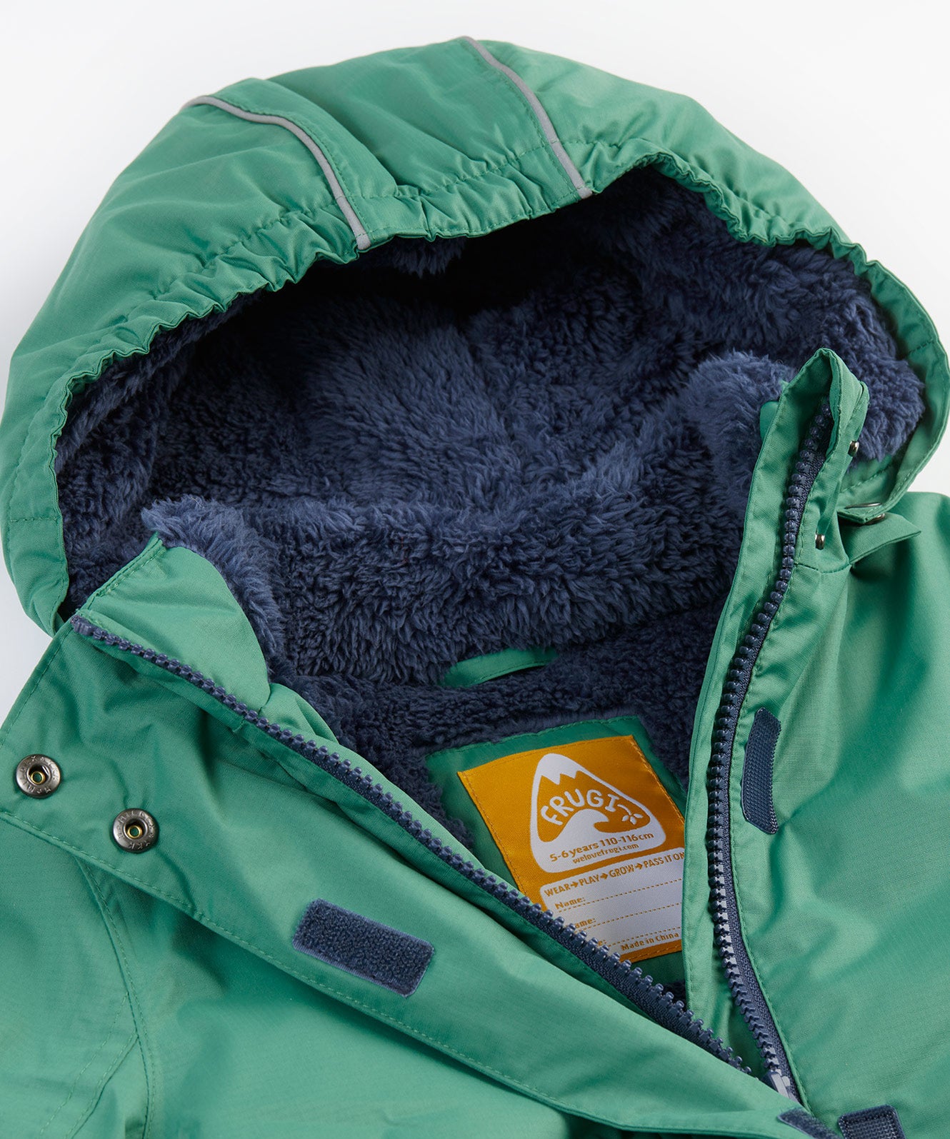 A close up of the Frugi kids snow and ski coat in green with a mountain scene print. Showing the thick navy fleece inner on the hood and zip detail