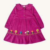 Frugi kids holly dress in damson flowers available at Babipur. A 100% GOTS organic cotton corduroy dress in bright purple with flower appliques on the skirt. Features a frilled collar and button fasteners.