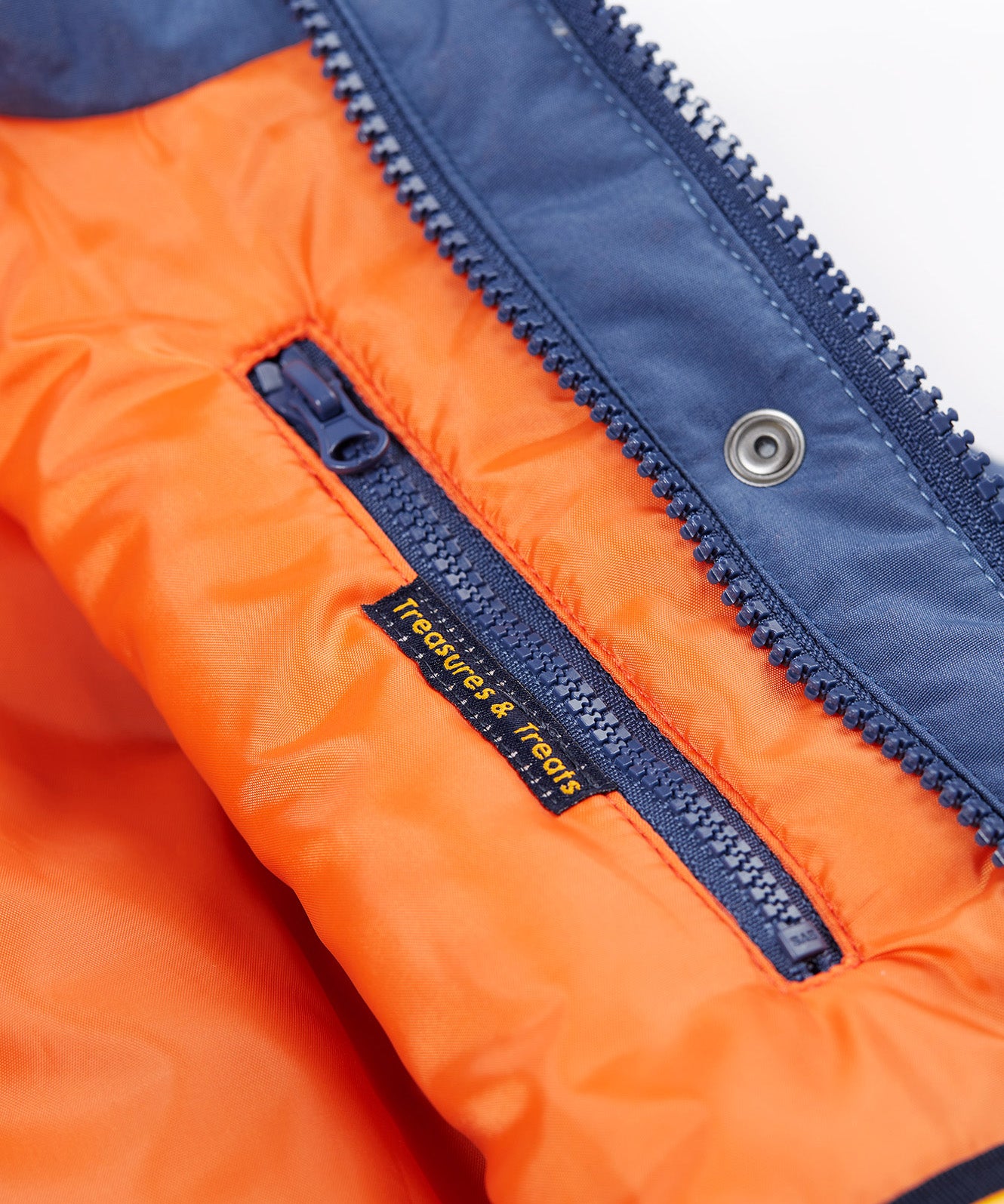 A close up of the Frugi kids 3 in 1 rambler coat in Autumn stripe /navy colourway showing the hidden side pocket and navy zip detail on the inside of the coat on orange post consumer recycled polyester fabric