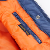 A close up of the Frugi kids 3 in 1 rambler coat in Autumn stripe /navy colourway showing the hidden side pocket and navy zip detail on the inside of the coat on orange post consumer recycled polyester fabric