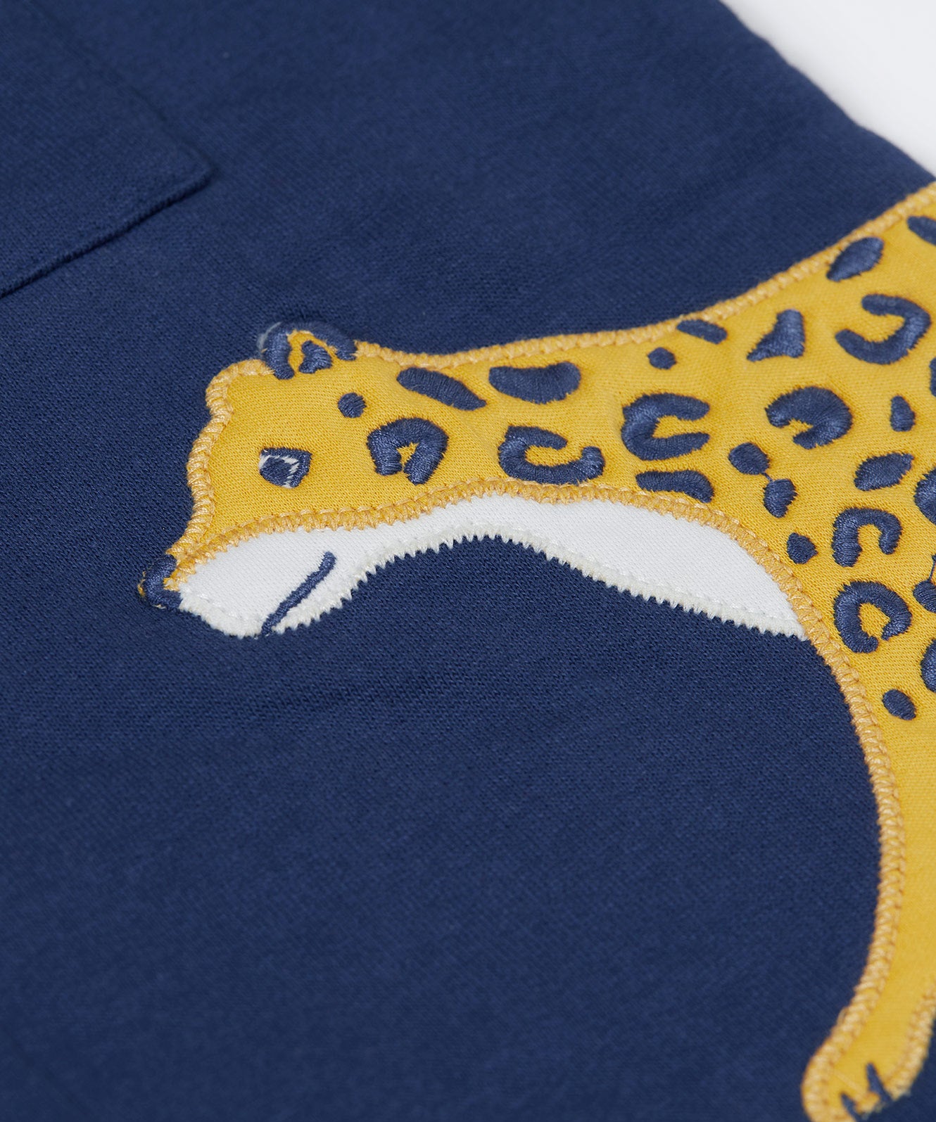 A close up of the yellow cheetah applique on the side of the Frugi Big Cats Navy Organic Cotton Cosy Kids' Shirt Shaket. This shaket has a tiger and cheetah applique details on the sides. This navy shirt jacket is a part of a wide range of organic cotton clothing for children available here at Babipur.