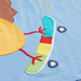Close up of the Frugi kids cornflower blue chicken t-shirt. Showing the appliqué detail of the skateboard on light blue organic cotton fabric