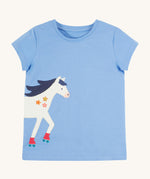 Frugi Elise Wrap Around T-Shirt in cornflower blue – GOTS organic cotton kids' t-shirt with short sleeves, featuring a playful appliqué of a white horse with roller skates that continues from the front to the back.