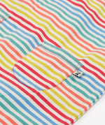 Close up of the Frugi kids cornflower rainbow stripe playsuit showing the small pocket detail on the front on striped organic cotton fabric.