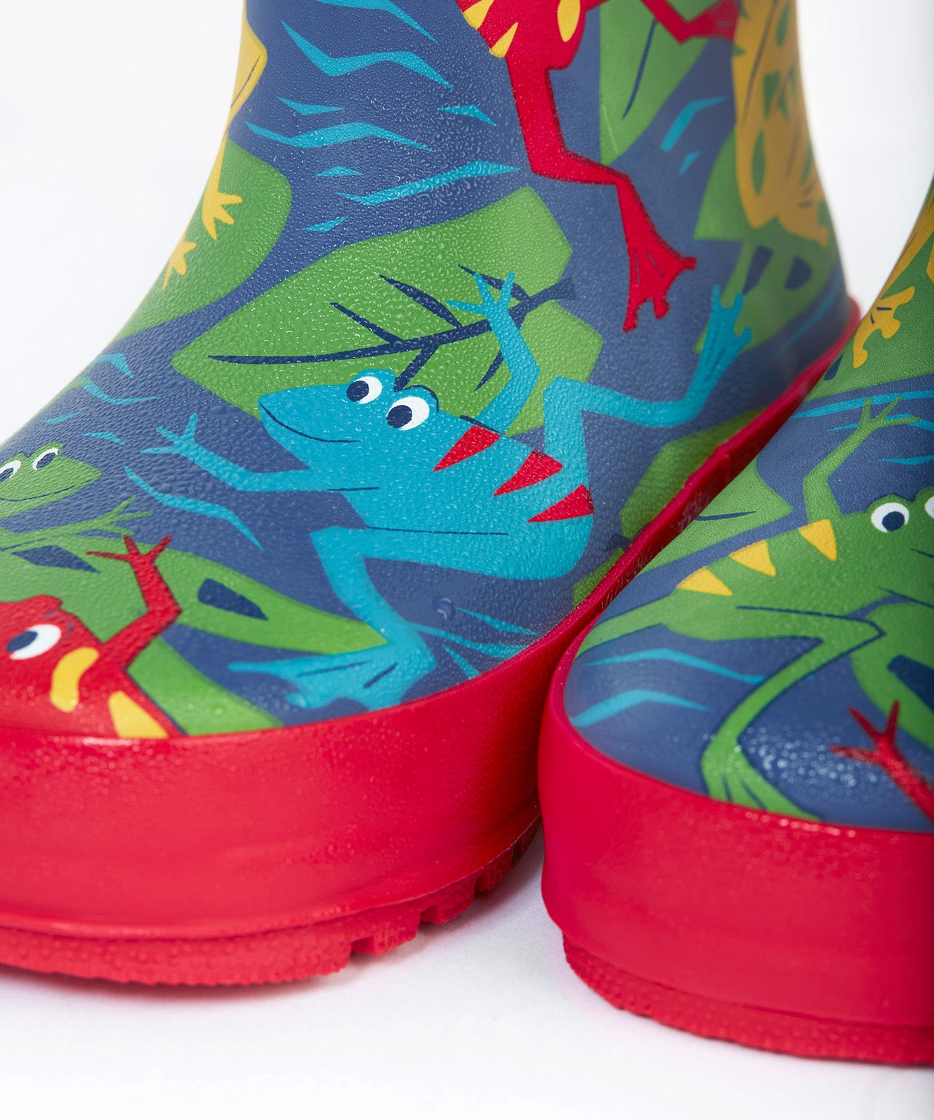 A close up of the bottom of the Frugi kids puddle buster wellington boots. Showing the the red trim and playful frog print detail on navy natural rubber material.