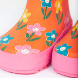 A close up of the bottom of the Frugi kids puddle buster wellington boots. Showing the the pink trim and playful flower print detail on orange natural rubber material.