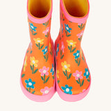 A top down view of the Frugi kids puddle buster wellington boots Showing the the pink trim and playful flower print detail on orange natural rubber material.