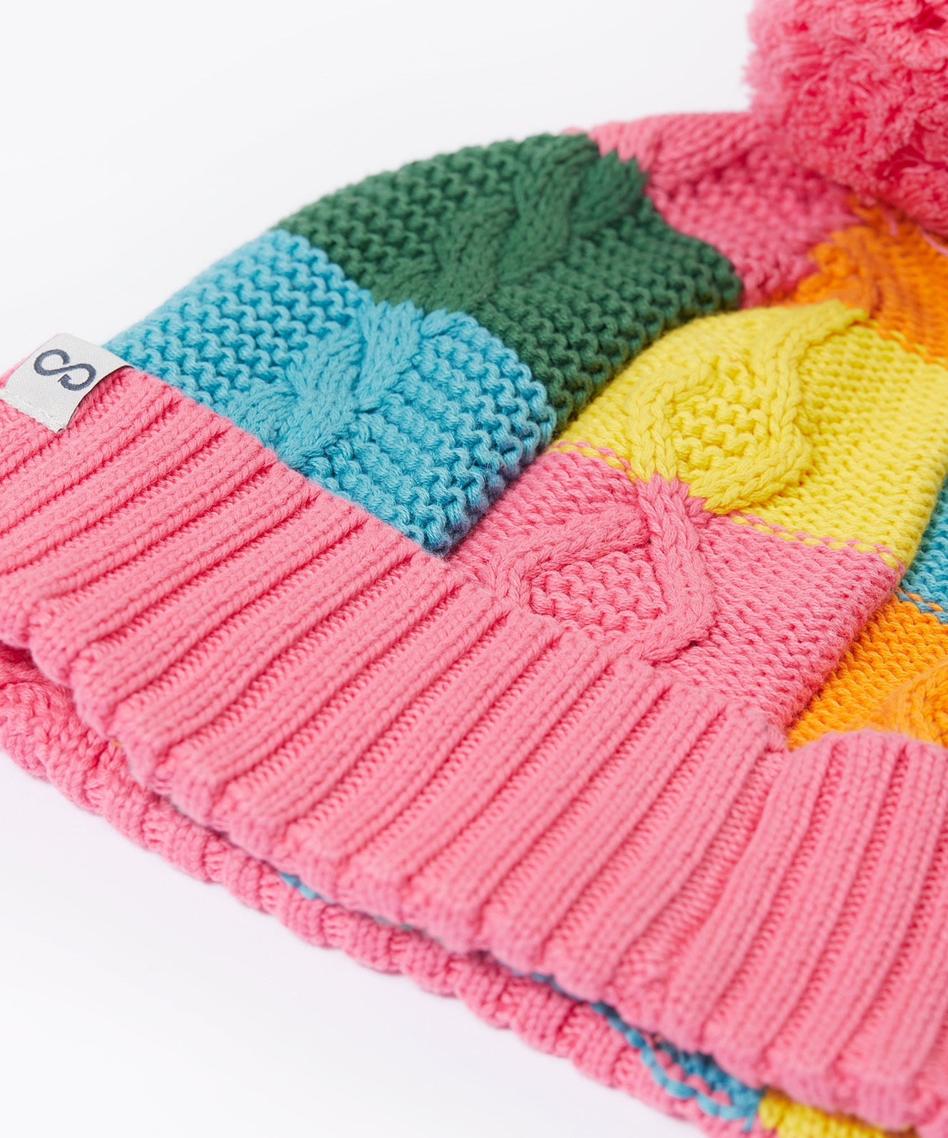 A close up of the Frugi kids cable knit rainbow check bobble hat. Showing the thick cable knit and pink turned up cuff