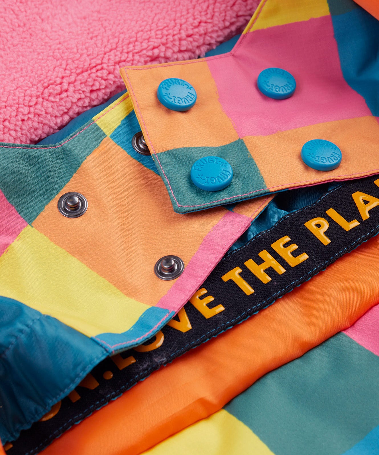 A close up of the Frugi kids snow and ski coat in rainbow check showing the snow skirt detail in matching rainbow check design and blue popper fasteners