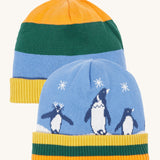 Frugi reversible voyager hat in penguin/ rainbow. A GOTS organic cotton cosy hat with a cute penguin design on blue with a yelow, green and orange striped ribbed trim and a matching bold stripe on the reverse side.