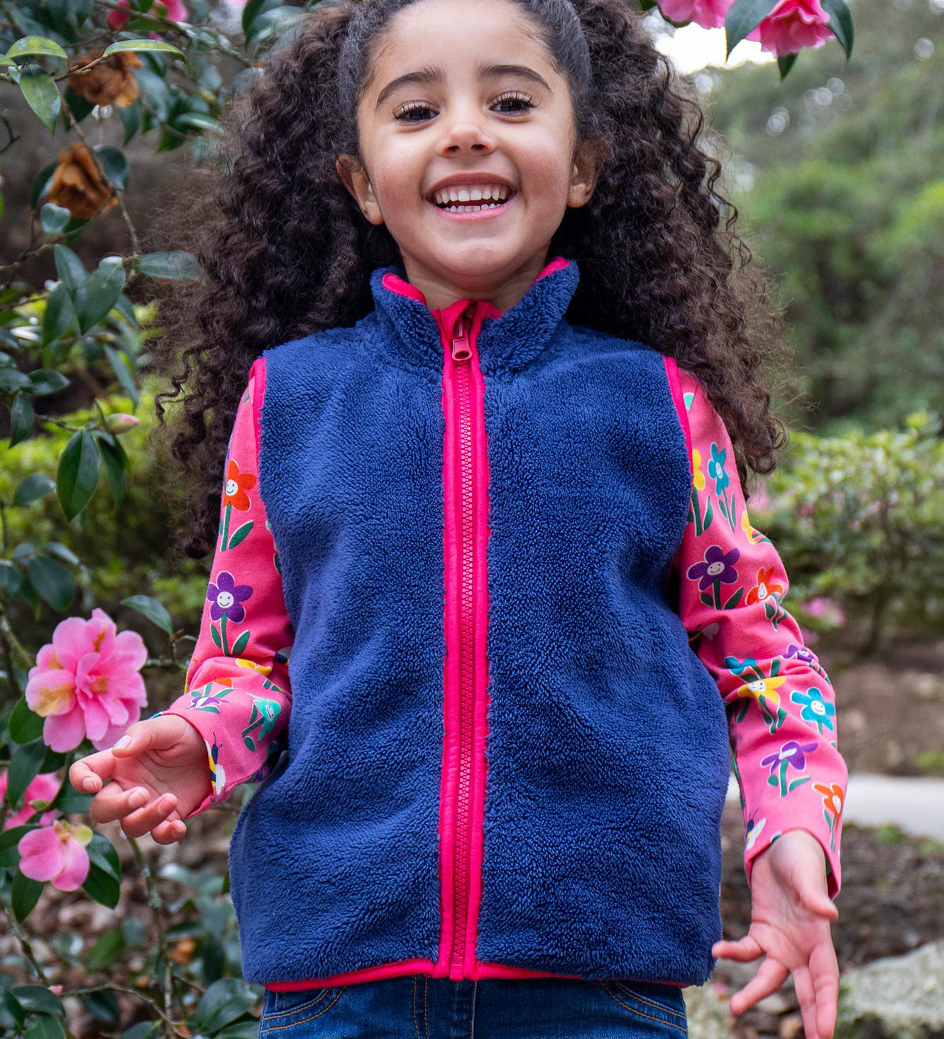 A child wearing the Frugi navy fleece gilet from the snapdragon/navy waterproof rambler 3 in 1 coat. A removable fleece gilet in navy with a pink zip and trim.