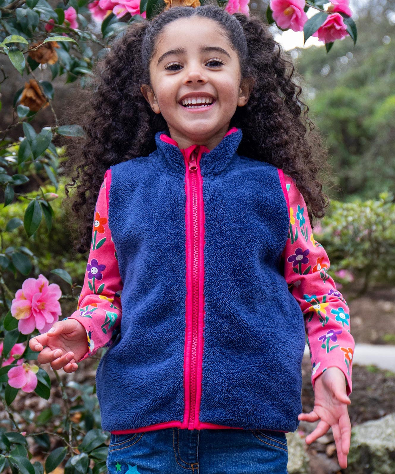 A child wearing the Frugi navy fleece gilet from the snapdragon/navy waterproof rambler 3 in 1 coat. A removable fleece gilet in navy with a pink zip and trim.