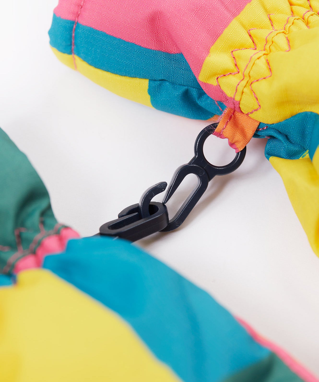 A close up of the Frugi kids rainbow check snow mittens showing the black clip detail on each mitten that can be attached on a ski coat.