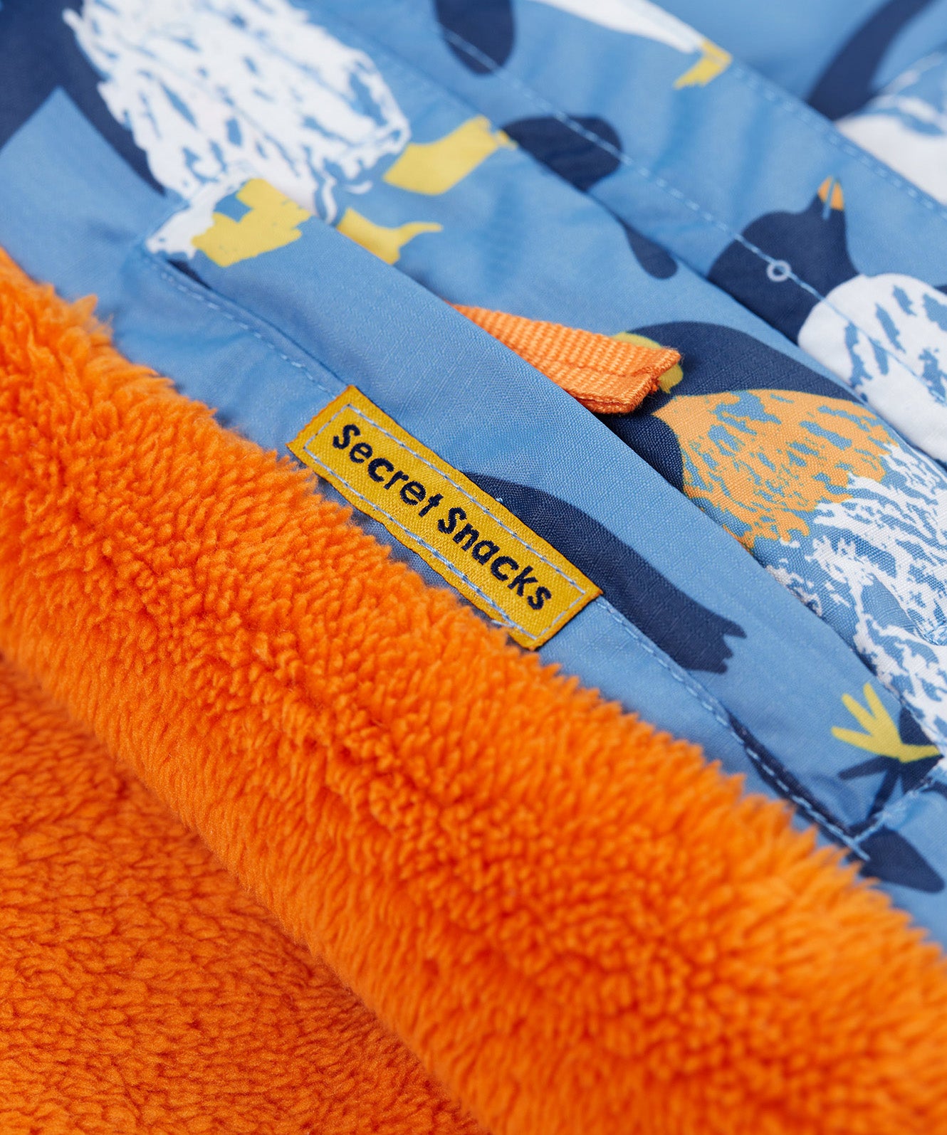 A close up of the Frugi kids snow and ski coat in penguin waddle showing the hidden pocket on the inside and orange fleece detail