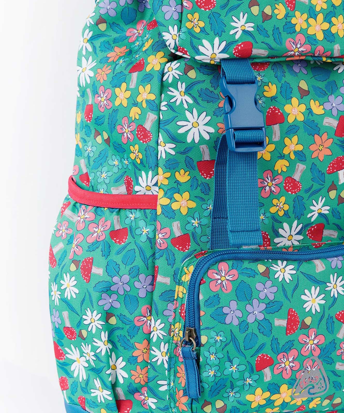 A close up of the Frugi kids trail blazing backpack in wild woods. Showing blue buckle for the flip top  and bottle holder detail