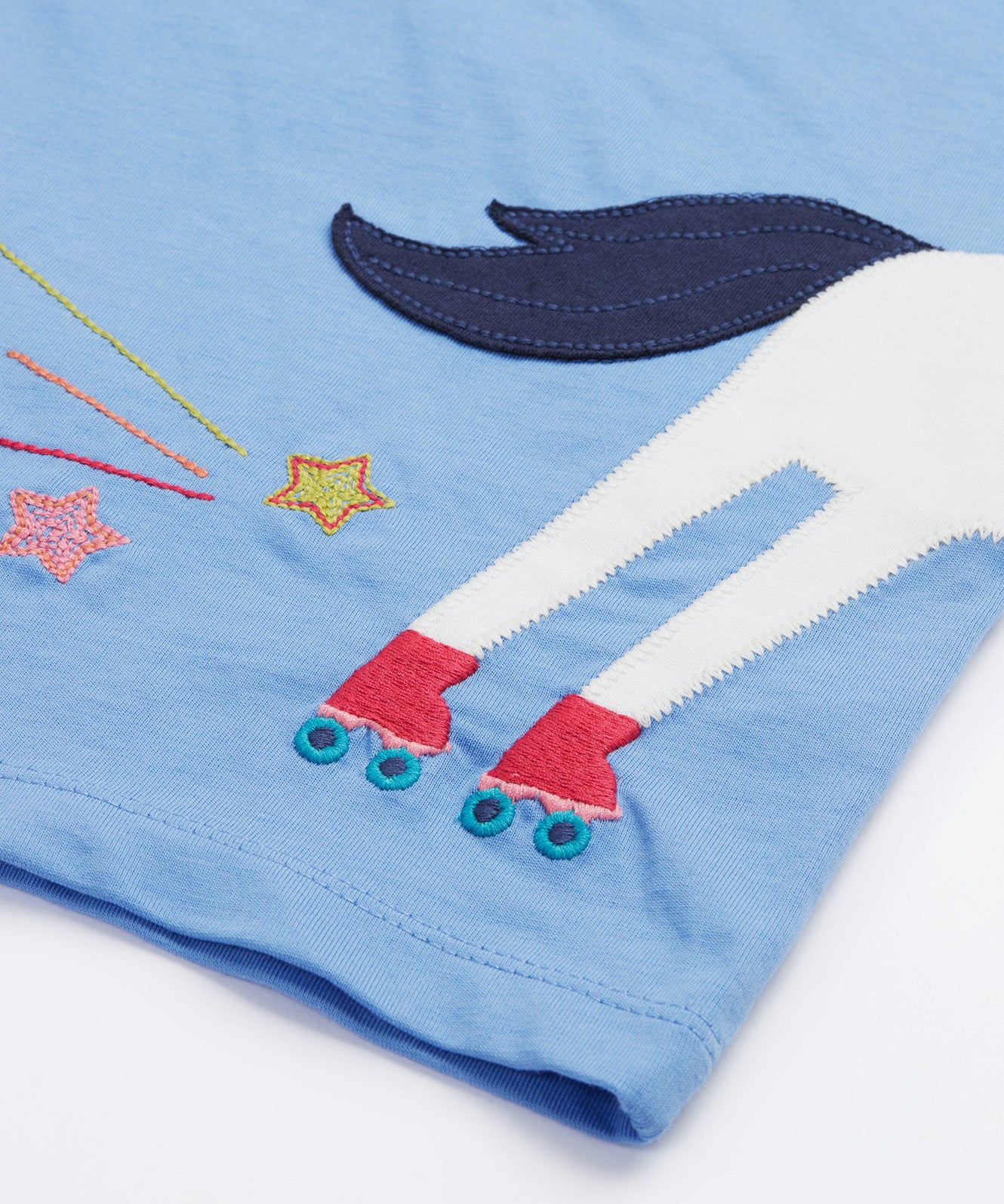 Back view of the Frugi Elise Wrap Around T-Shirt in cornflower blue – featuring the back of the white horse appliqué with roller skates and embroidered stars and trails. Made from GOTS organic cotton