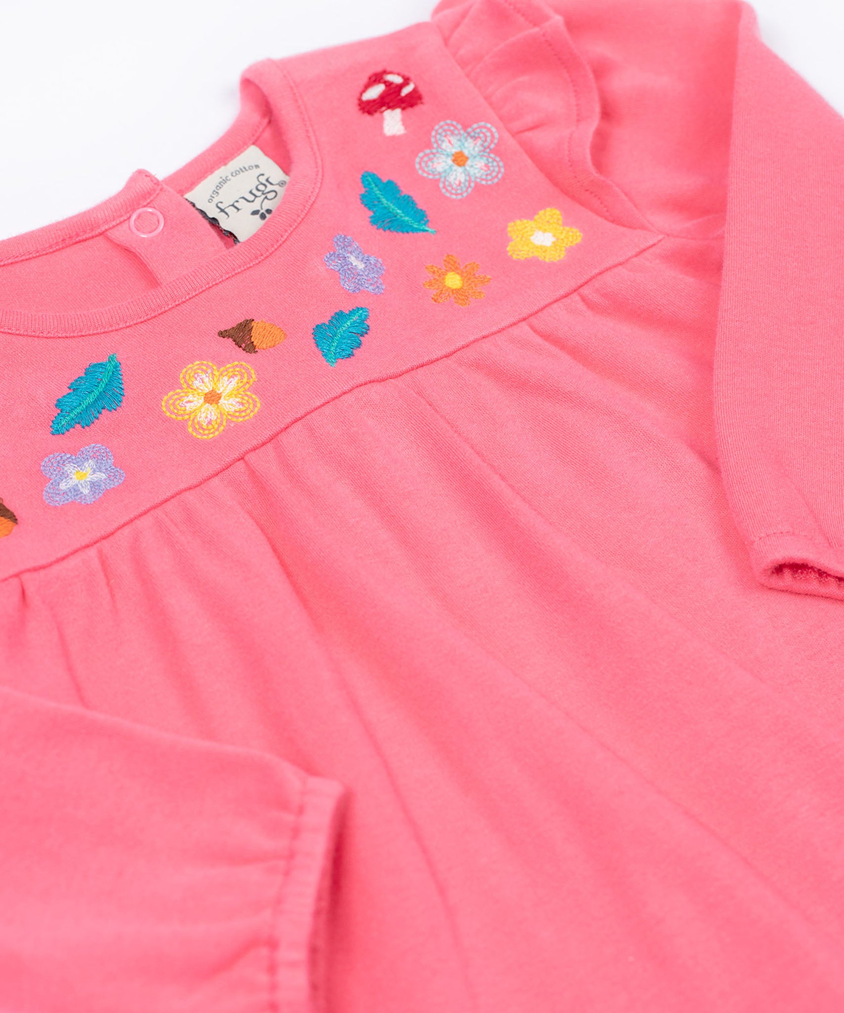 A close up of the Frugi kids kyla outfit in tulip/wild woods showing the long sleeves pink top with frilled shoulders. Features woodland themed embroidery.