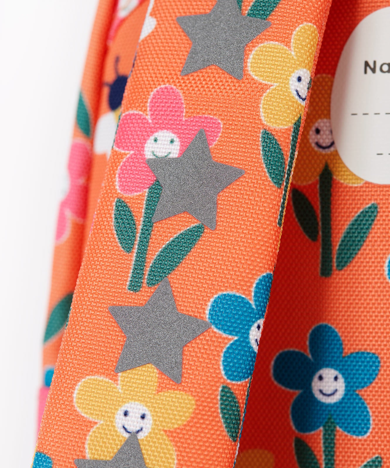 A close up of the shoulder strap of the Frugi little adventures fun flowers backpack showing the reflective stars and flower print detail
