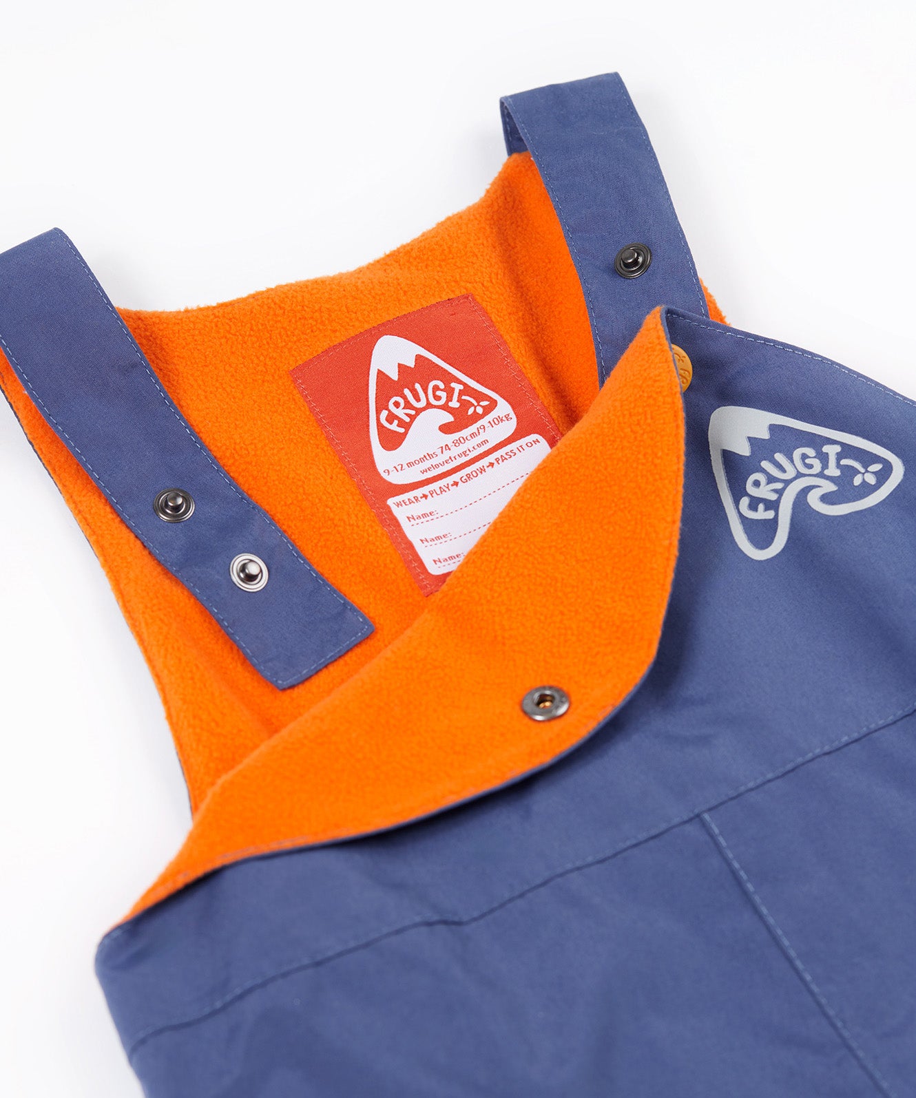 A close up of the Frugi little kids waterproof dungarees in navy showing the popper detail for adjusting the size. Features a orange fleece inner liner for warmth and a name tag stitched on the inside.