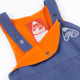 A close up of the Frugi little kids waterproof dungarees in navy showing the popper detail for adjusting the size. Features a orange fleece inner liner for warmth and a name tag stitched on the inside.