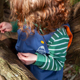 A close up of a toddler wearing the A toddler standing outside wearing the Frugi navy waterproof dungarees showing the yellow popper and orange fleece detail