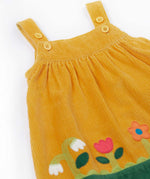 A close up of the front of the Frugi Nellie Organic Cotton yellow gold Corduroy Pinafore Dress with Flowers. This dress is a part of a wide range of organic cotton clothing for children available here at Babipur.