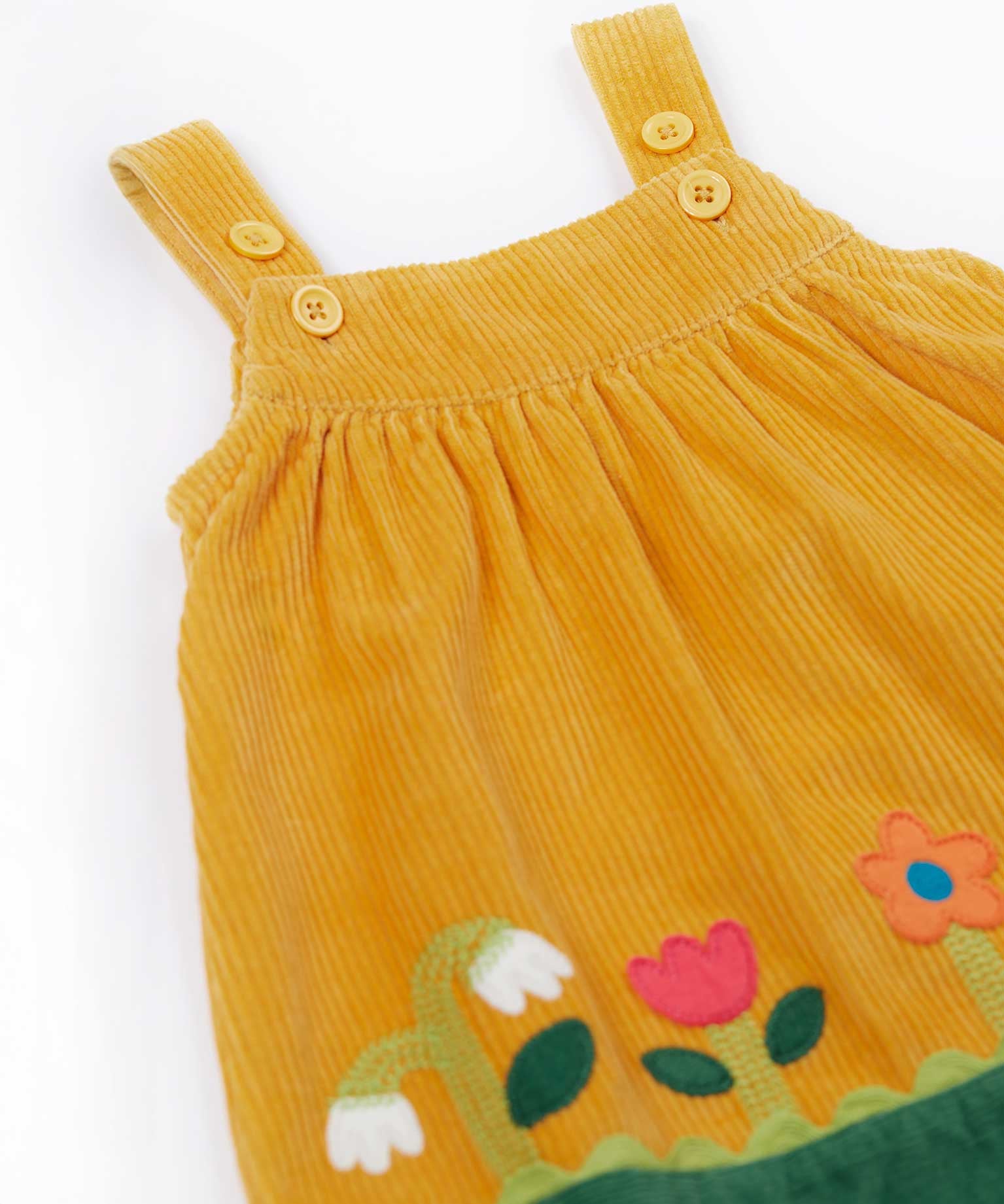 A close up of the front of the Frugi Nellie Organic Cotton yellow gold Corduroy Pinafore Dress with Flowers. This dress is a part of a wide range of organic cotton clothing for children available here at Babipur.